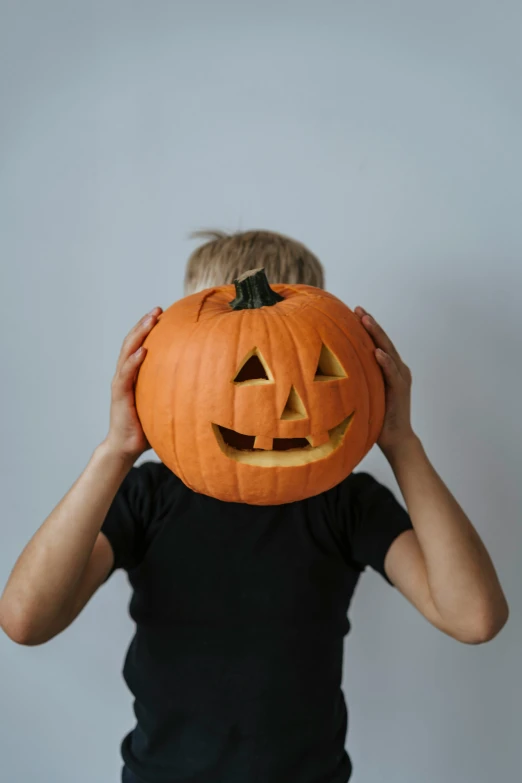 a young boy holding a pumpkin over his head, pexels, on a gray background, masked person in corner, profile image, uploaded