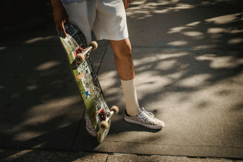 a man holding a skateboard on a sidewalk, pexels contest winner, white tights covered in stars, wearing golf shorts, gum rubber outsole, thumbnail