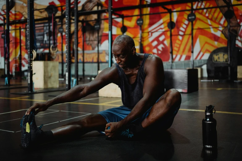 a man sitting on the ground in a gym, a portrait, by Matija Jama, pexels contest winner, lance reddick, pixeled stretching, thumbnail, background image