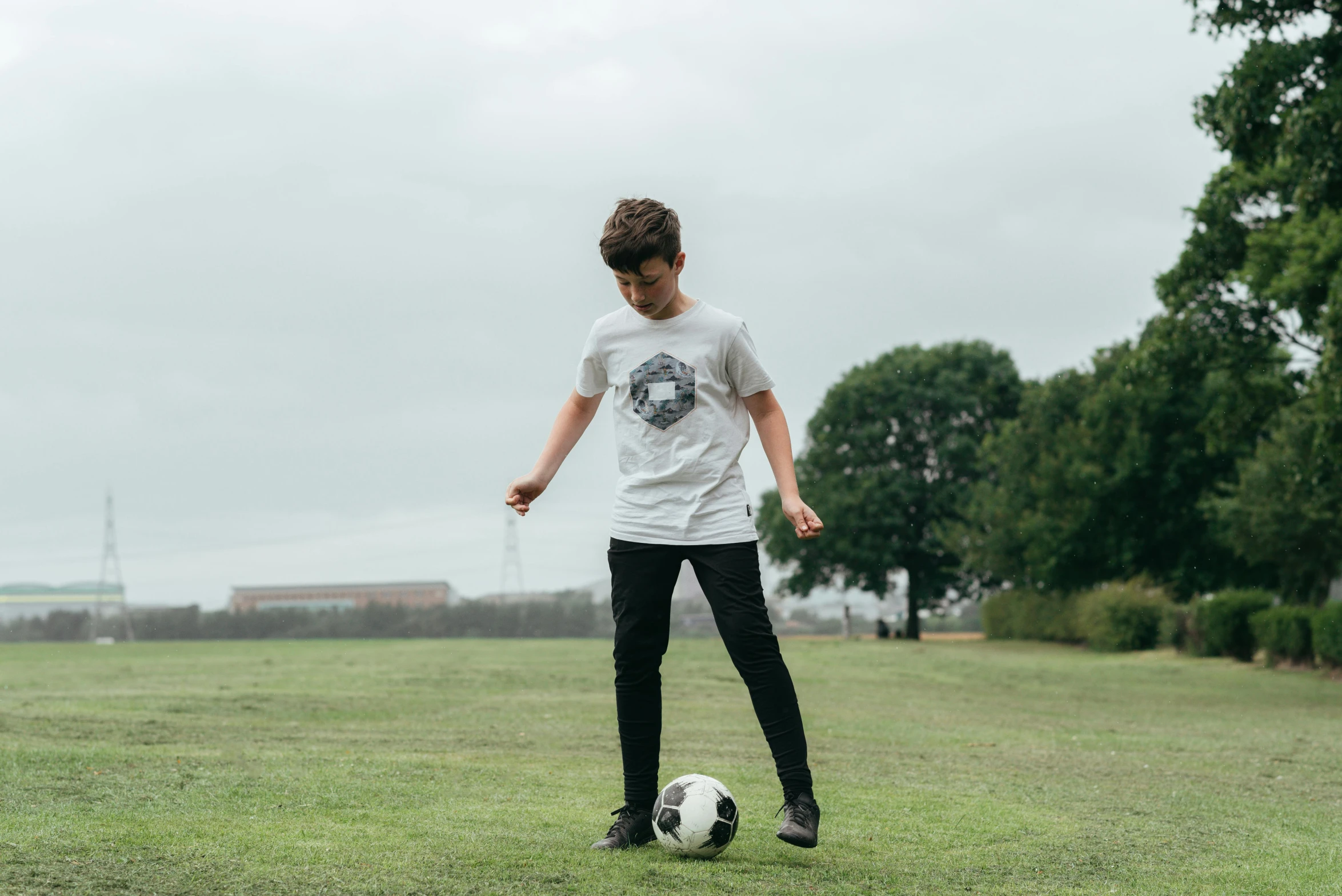 a young boy kicking a soccer ball on a field, inspired by Andrew Robertson, pexels contest winner, happening, printed on a cream linen t-shirt, outlive streetwear collection, grey, aged 13