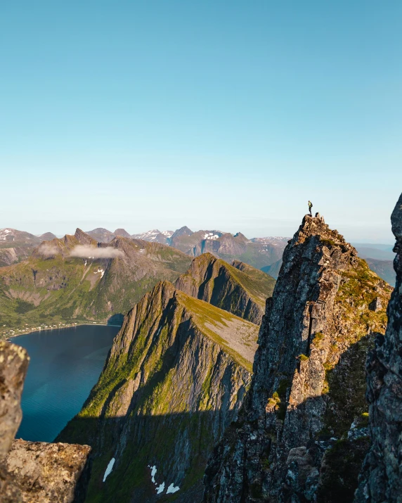 a man standing on top of a mountain next to a lake, by Jesper Knudsen, pexels contest winner, two mountains in background, nordic summer, conde nast traveler photo, rock climbing