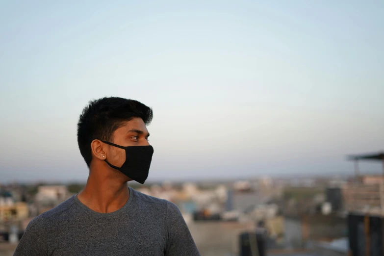 a man standing on top of a roof wearing a face mask, a picture, happening, profile image, ayan nag, with slight stubble, black