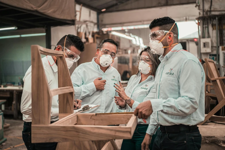 a group of people standing around a piece of wood, in a factory, people are wearing masks, wooden furniture, profile image