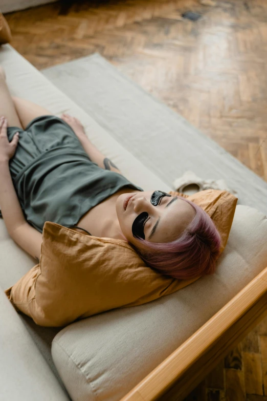 a woman laying on top of a bed on a hard wood floor, inspired by Elsa Bleda, trending on pexels, relaxing on a modern couch, woman with rose tinted glasses, ocher, laying back on a pillow