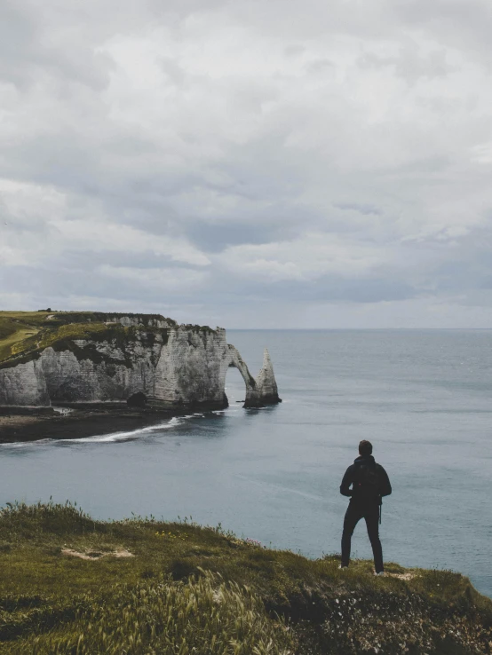 a person standing on a cliff overlooking a body of water, northern france, epic land formations, 2019 trending photo, white stone arches