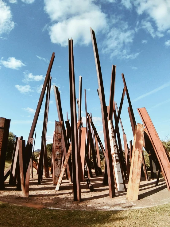 a group of wooden poles sitting on top of a grass covered field, an abstract sculpture, unsplash, land art, iron smelting pits, “ iron bark, various sizes, 1999 photograph