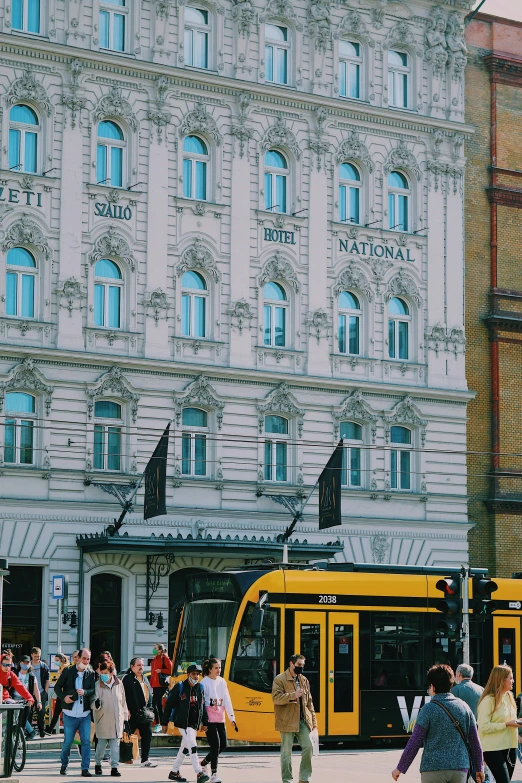 a yellow bus driving down a street next to tall buildings, by Nina Hamnett, pexels contest winner, art nouveau, helsinki, square, commercial banner, hotel