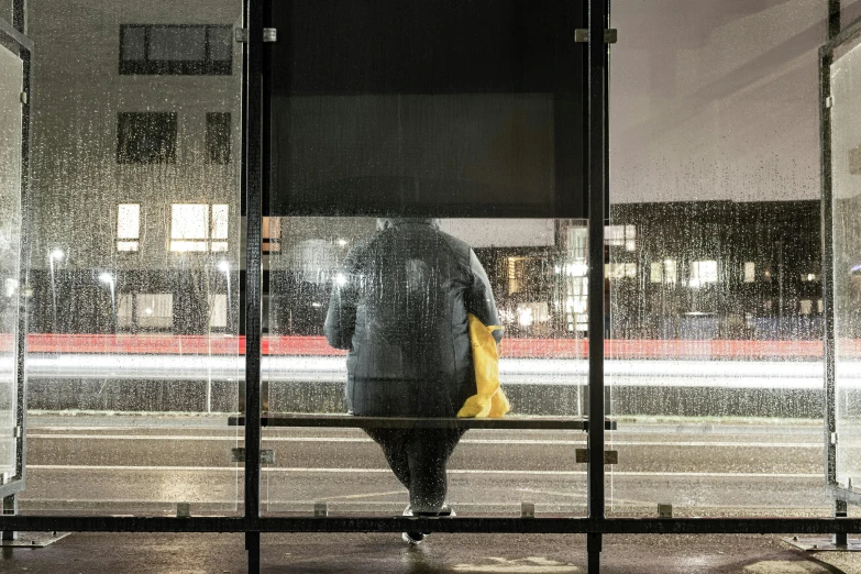 a person standing at a bus stop in the rain, a picture, inspired by Andreas Gursky, hyperrealism, obese ), with yellow cloths, facing away, tokujin yoshioka