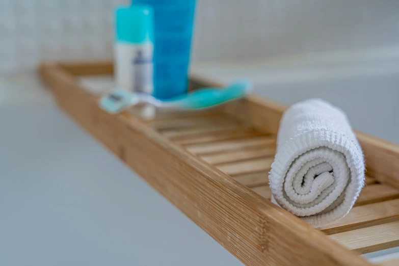 a wooden shelf holding two towels and a toothbrush, by Julian Allen, unsplash, bathtub, close up shot from the side, made of bamboo, detail shot