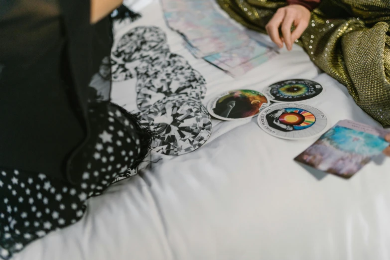 a woman laying on top of a bed covered in stickers, an album cover, by Julia Pishtar, trending on pexels, the phases of the moon, pair of keycards on table, esoteric clothing, detail shot