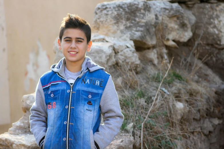 a young boy standing in front of a stone wall, a picture, pexels, les nabis, real life photo of a syrian man, portrait of 14 years old boy, 15081959 21121991 01012000 4k, outdoor photo