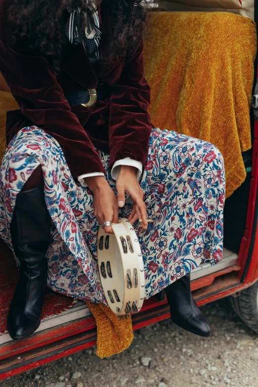 a woman sitting in the back of a van, an album cover, by Nina Hamnett, trending on pexels, dressed in long fluent skirt, paisley, detail shot, bongos