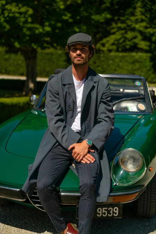 a man sitting on top of a green car, trench coat and suit, in gunmetal grey, de tomaso, style of gilles beloeil