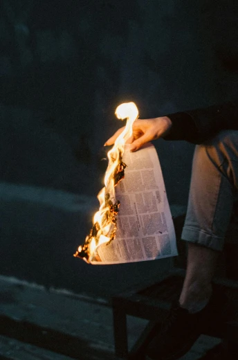 a person sitting on a bench holding a lit newspaper, by Sebastian Spreng, trending on unsplash, renaissance, standing in fire, burnt paper, light casting onto the ground, ignant