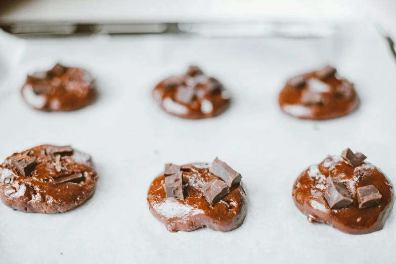 a close up of chocolate cookies on a baking sheet, a portrait, unsplash, on a pale background, background image, liam brazier, glazed