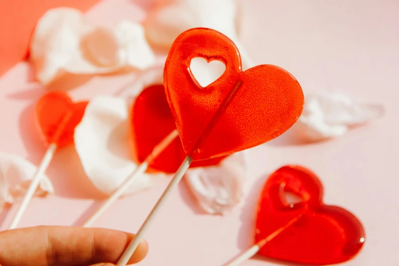 a person holding a heart shaped lollipop on a stick, by Julia Pishtar, trending on pexels, carved soap, red and white neon, chiffon, thumbnail