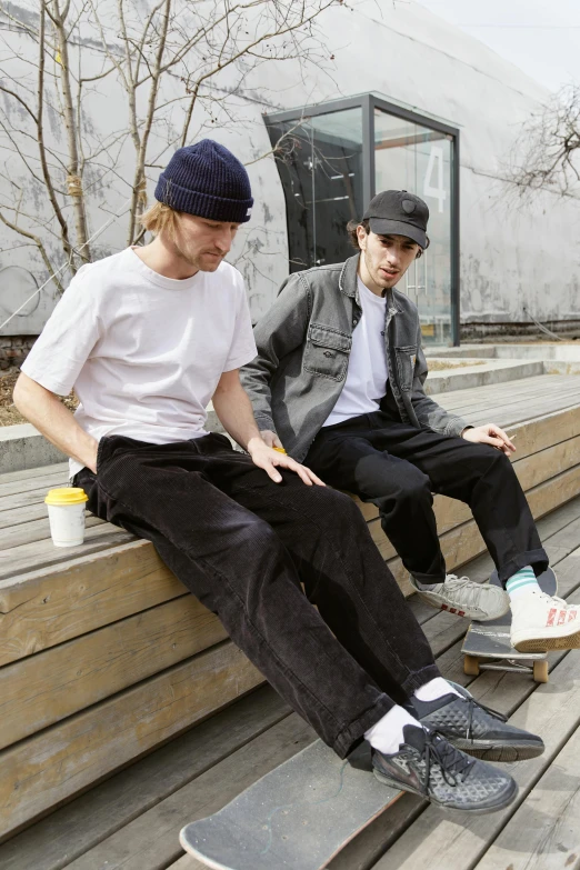 a couple of men sitting on top of a wooden bench, baggy black pants, skateboarder style, corduroy, federation clothing