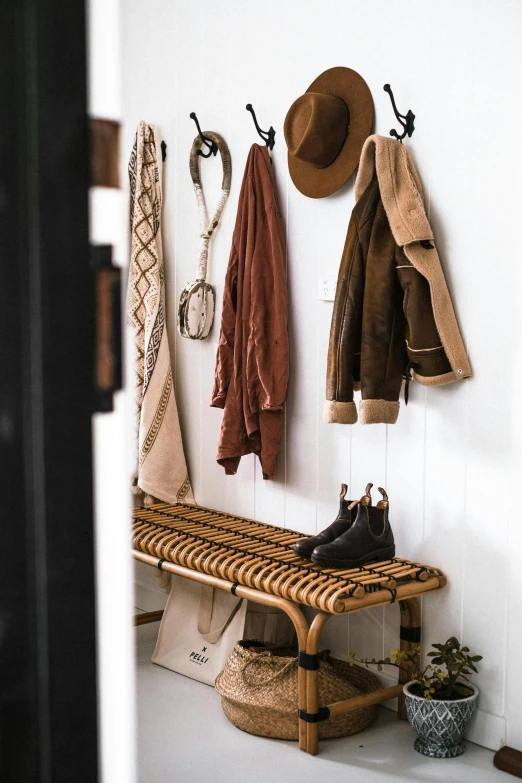 a wooden bench sitting next to a white wall, by Nicolette Macnamara, trending on unsplash, straw hat and overcoat, leather clothing and boots, home display, shepherd's crook