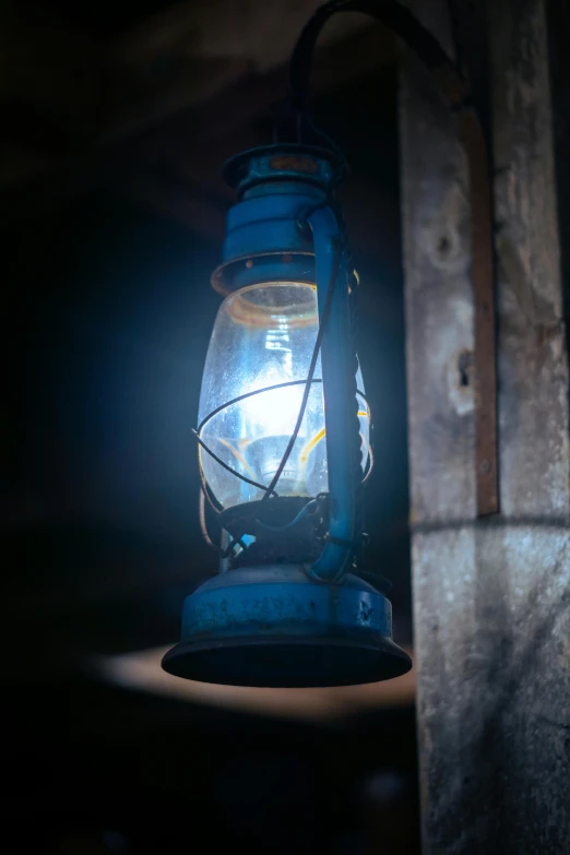 a blue lantern sitting on top of a wooden pole, a portrait, inspired by Carl Spitzweg, unsplash, in an abandoned barn, electrifying, close-up photograph, 2019 trending photo