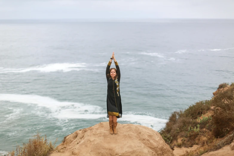 a woman standing on top of a rock near the ocean, arabesque, wearing dark green robes, bay area, celebrating, icon