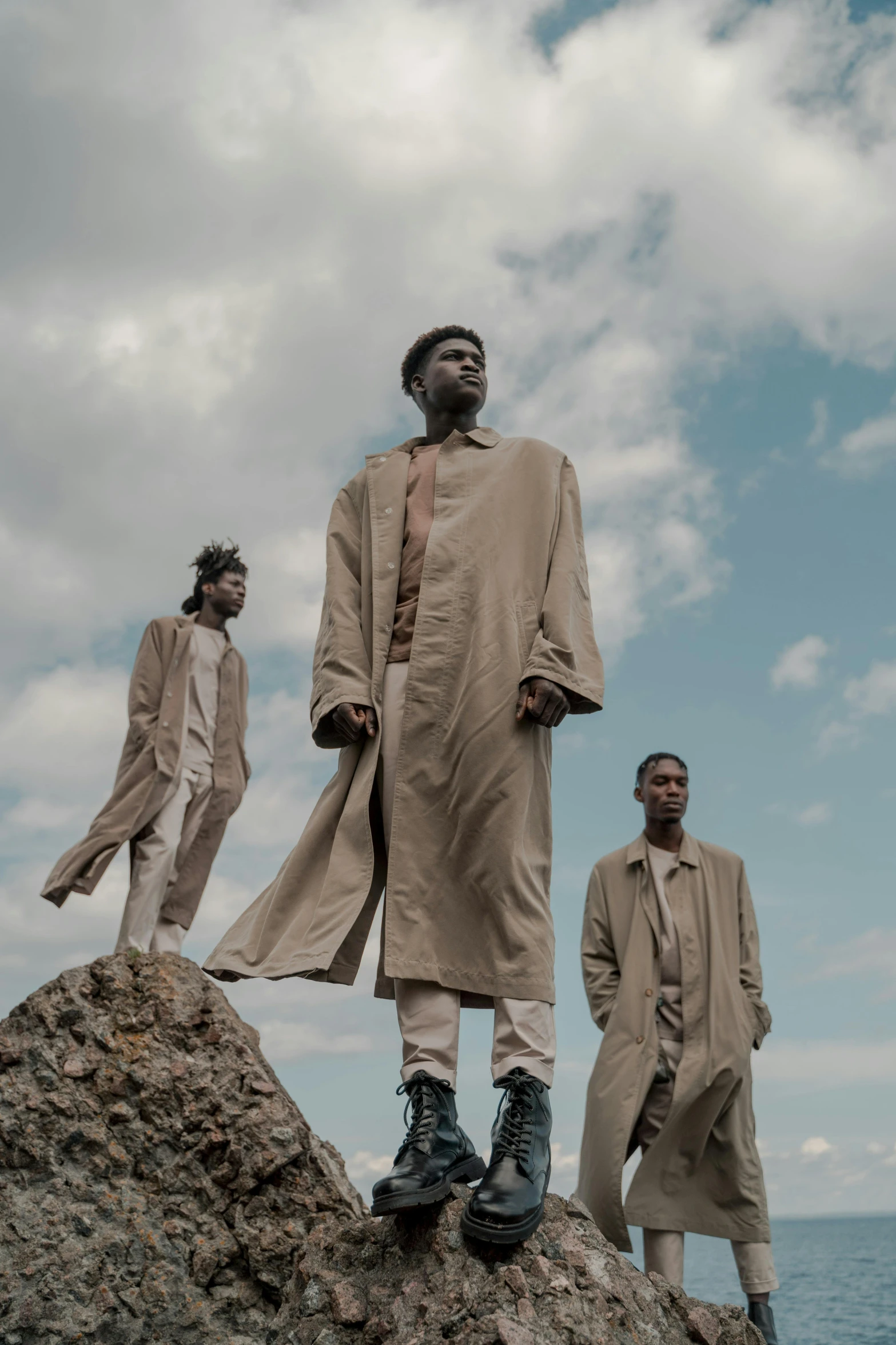 a group of men standing on top of a rock, an album cover, unsplash, afrofuturism, wearing a duster coat, adut akech, ( ( theatrical ) ), brown