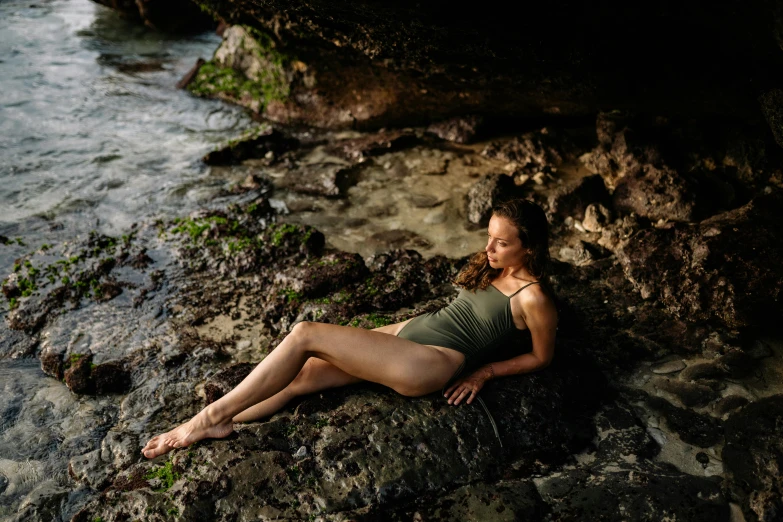 a woman laying on a rock next to a body of water, avatar image