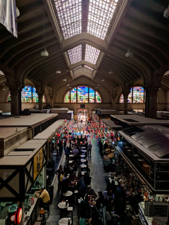 a large room filled with lots of people, by Meredith Dillman, pexels contest winner, large stained glass windows, colored market stand, train station, thumbnail