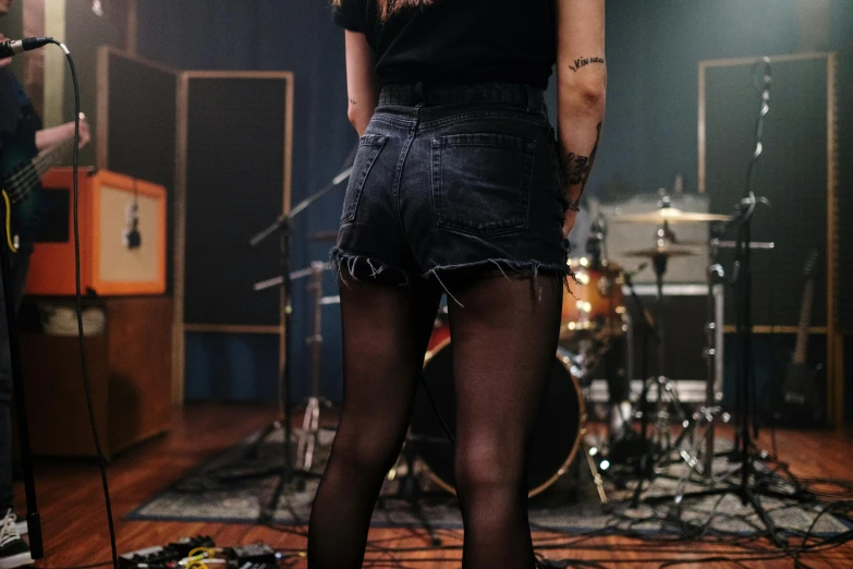 a woman that is standing in front of a microphone, an album cover, inspired by Elsa Bleda, trending on pexels, denim hot-pants, epk, wearing black shorts, backview