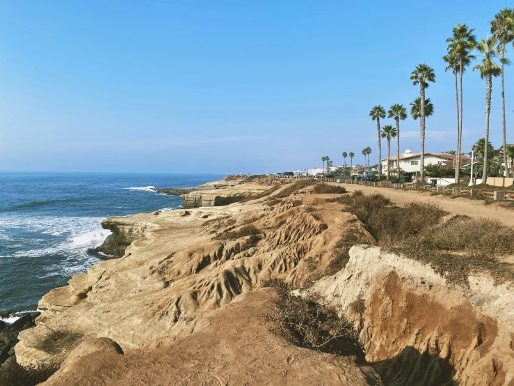 a man standing on top of a cliff next to the ocean, unsplash, photorealism, dried palmtrees, stephen shore, summer street near a beach, erosion