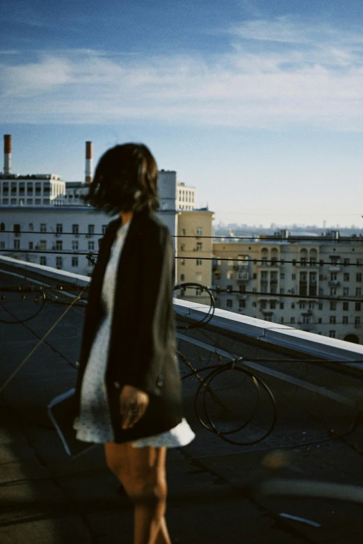 a woman standing on top of a roof next to a building, inspired by Anka Zhuravleva, unsplash, short skirt and a long jacket, distant - mid - shot, walking to the right, ignant