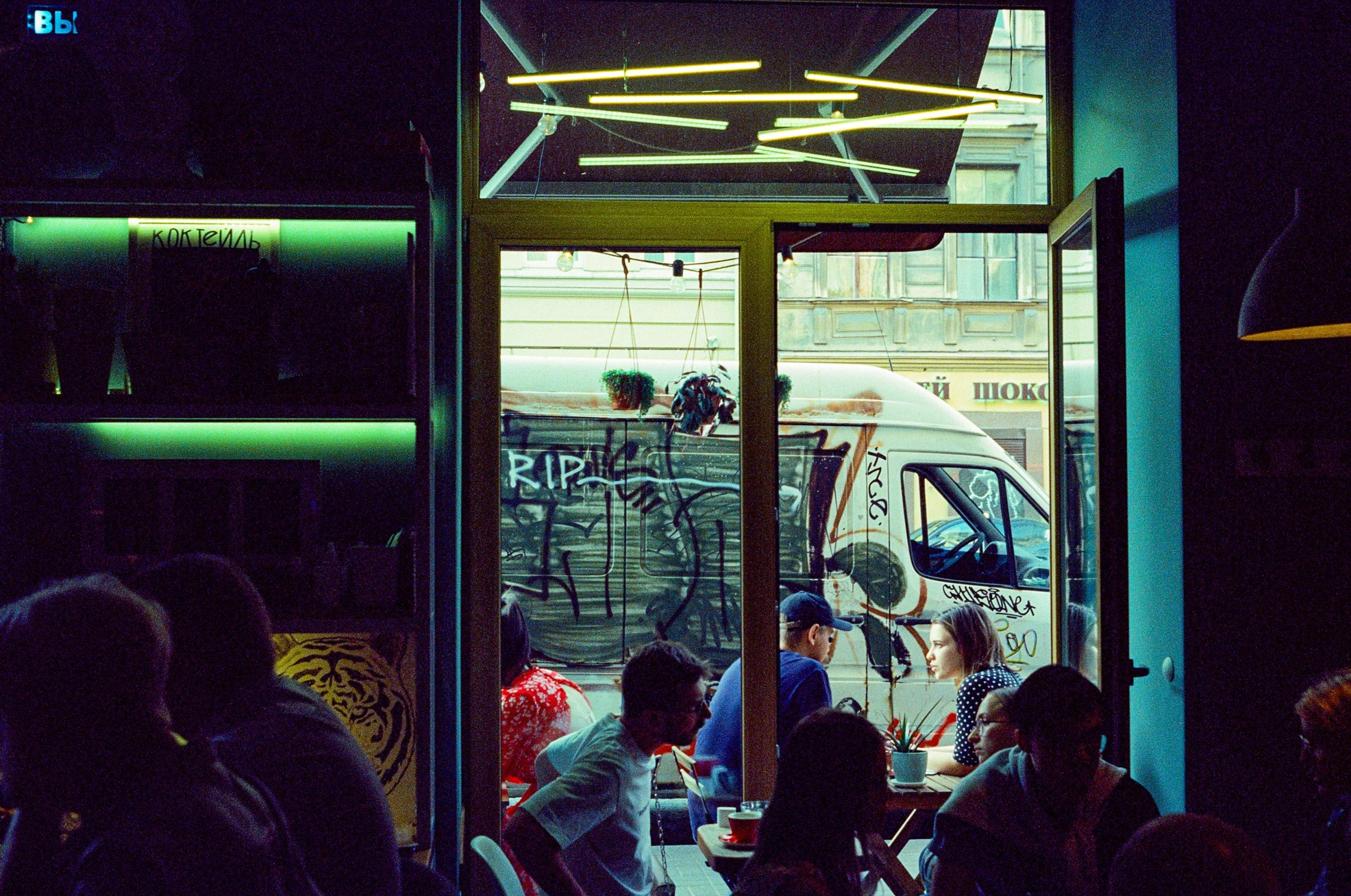 a group of people sitting at a table in a restaurant, a photo, inspired by Elsa Bleda, fantastic realism, tel aviv street, melbourne, seen from outside, lomography