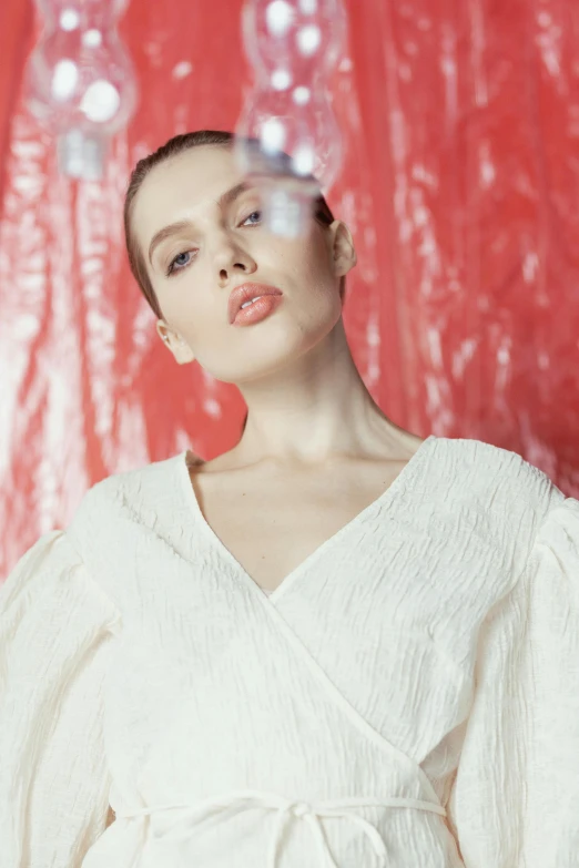 a woman standing in front of a red backdrop, inspired by Lili Árkayné Sztehló, trending on pexels, bauhaus, wearing white silk robe, wet look, voluminous sleeves, off - white collection