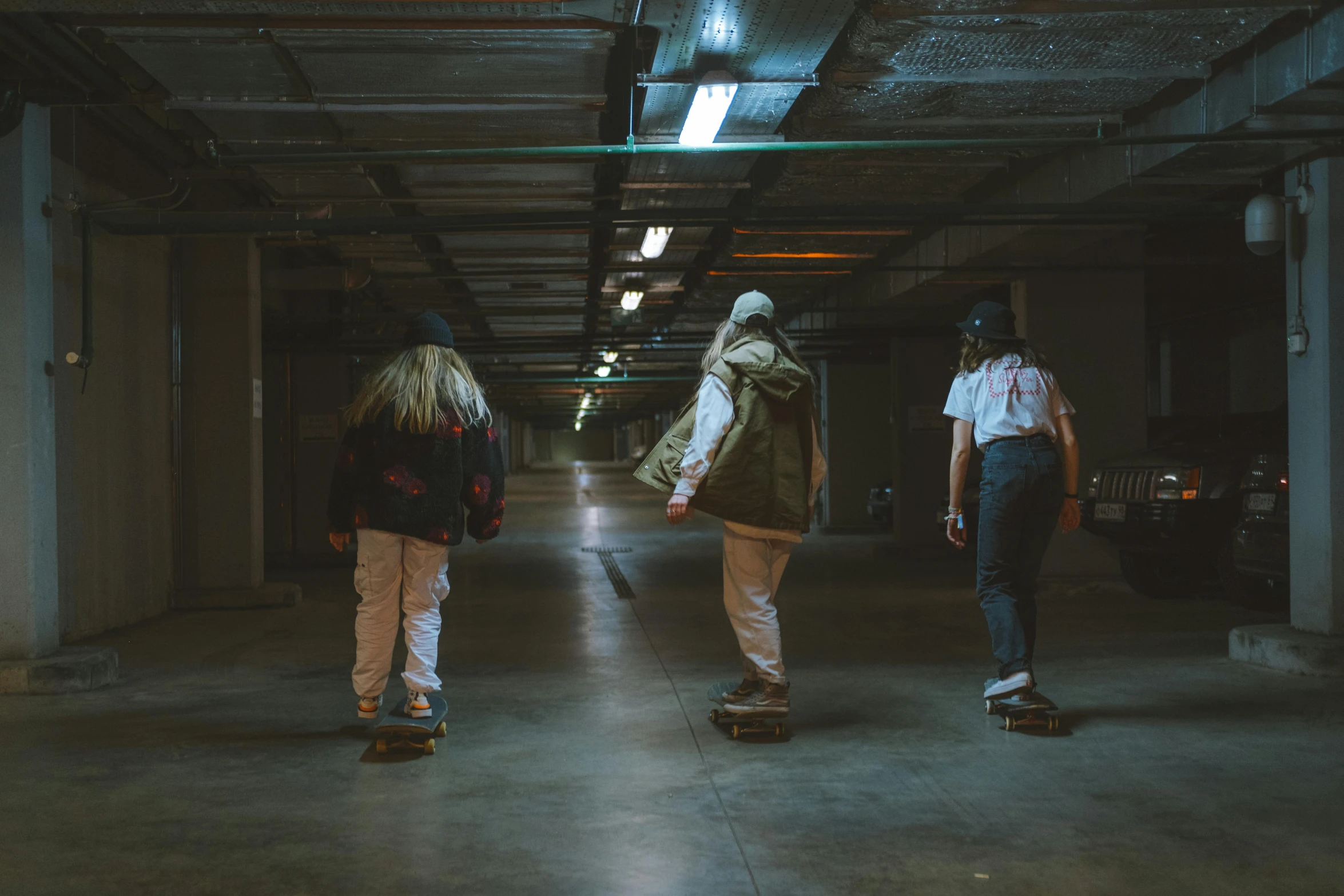 a group of people riding skateboards in a parking garage, inspired by Elsa Bleda, unsplash contest winner, creepy themed, cinematic outfit photo, young girls, medium shot taken from behind