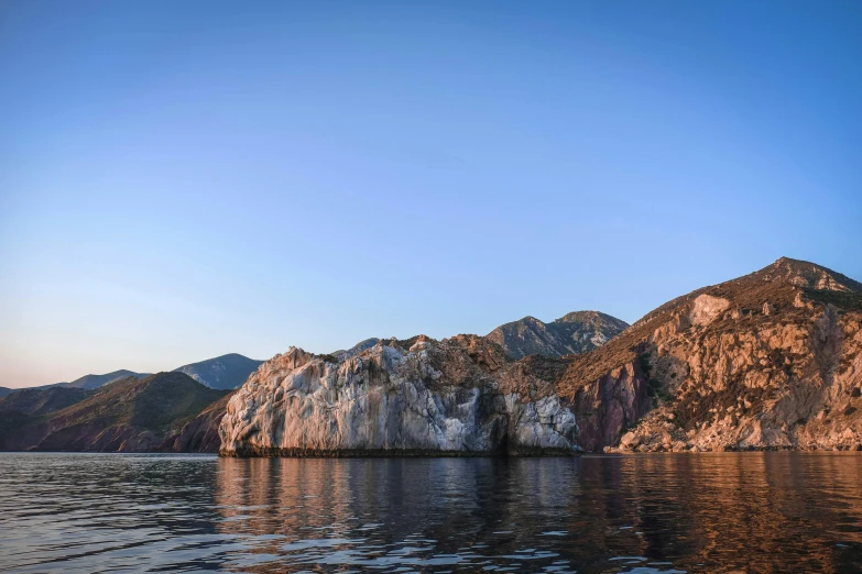 a body of water with mountains in the background, a picture, coastal cliffs, dappled in evening light, conde nast traveler photo, geology