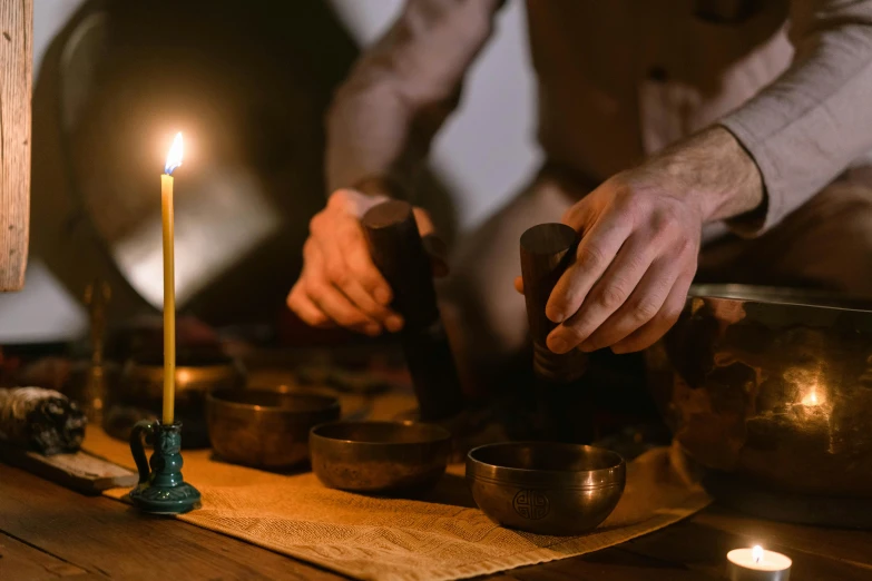 a man lighting a candle in front of a set of singing bowls, trending on pexels, lachlan bailey, mortar and pestle, brown