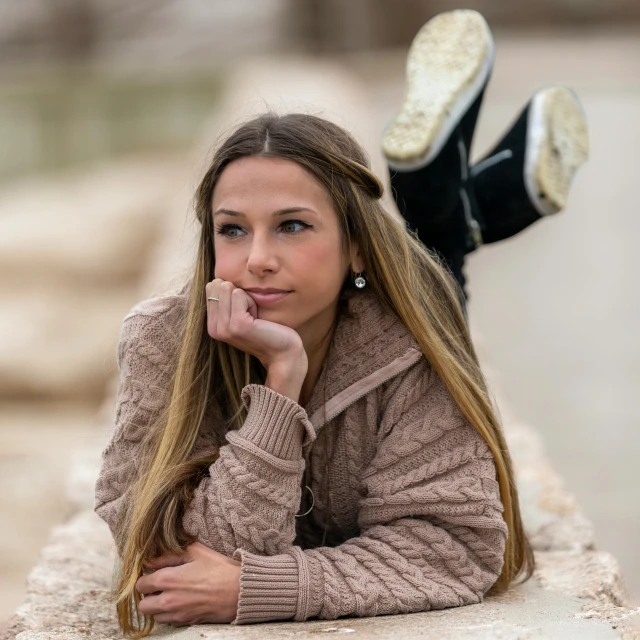 a beautiful young woman laying on top of a stone wall, a portrait, trending on pexels, realism, she wears boots, thinking pose, beautiful jewish woman, wearing a sweater