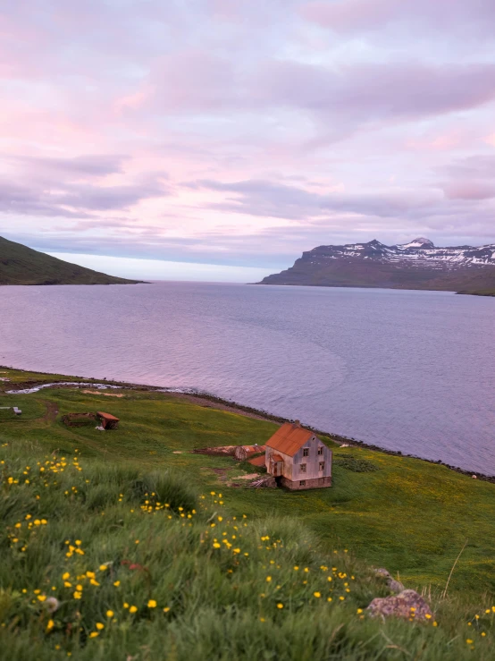 a small house sitting on top of a lush green hillside, by Daren Bader, pexels contest winner, in the iceland calm water, at gentle dawn pink light, faroe, panoramic view
