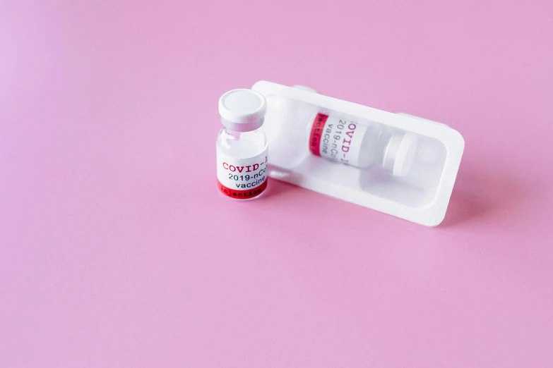 a pill case sitting on top of a pink surface, by Olivia Peguero, pexels contest winner, white and red color scheme, syringe, coronavirus, cosmopolitan