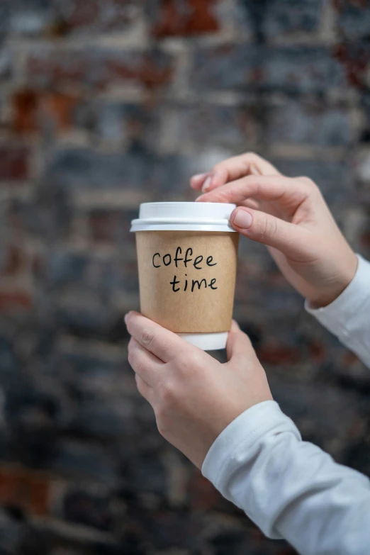 a person holding a cup of coffee in front of a brick wall, detailed product image, good times, label, hands on counter