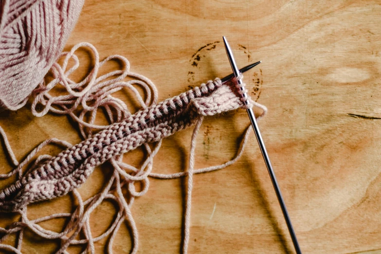 a close up of yarn and knitting needles on a wooden surface, inspired by W. Lindsay Cable, trending on pexels, process art, brown and pink color scheme, wielding a crowbar, animation, surgery