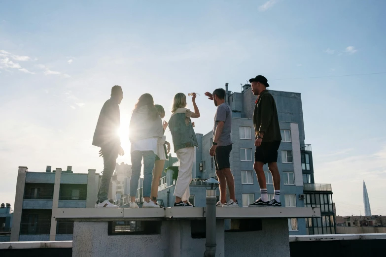 a group of people standing on top of a building, by Niko Henrichon, pexels contest winner, rooftop party, sun drenched, looking to the side, blank