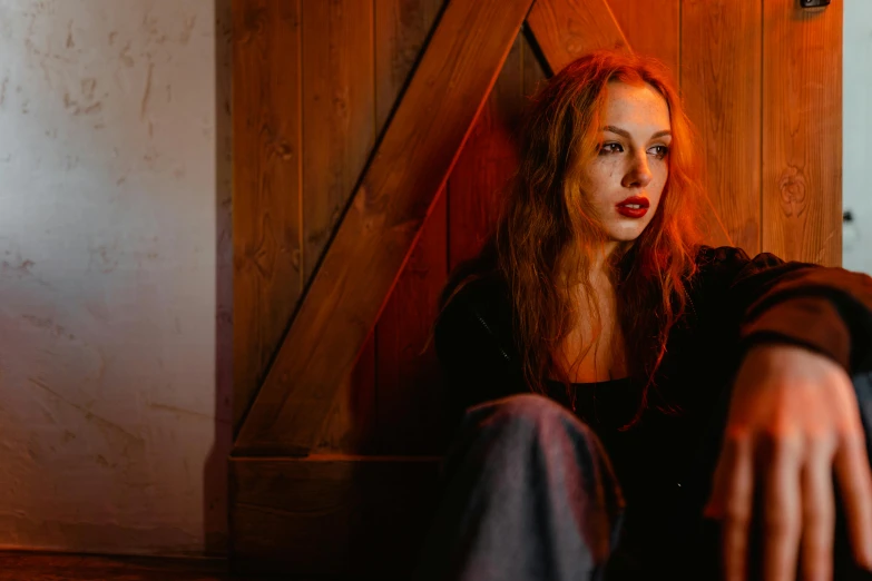 a woman sitting in front of a wooden door, inspired by Nan Goldin, pexels contest winner, antipodeans, sophie turner, hr ginger, portrait sophie mudd, against a red curtain