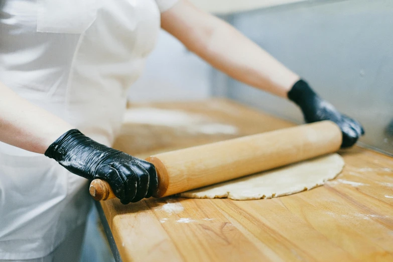 a woman rolling out dough on a wooden table, trending on pexels, fantasy bakery, wearing gloves, thumbnail, mechanics