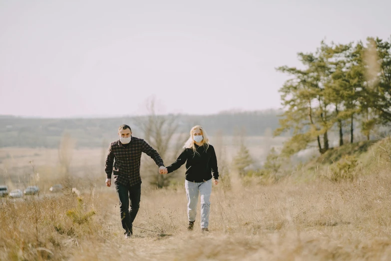 a man and woman walking in a field holding hands, a photo, pexels, face mask, hunting, knee, instagram picture