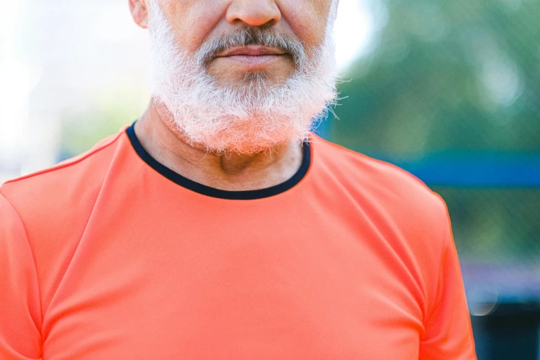 a man in an orange shirt holding a tennis racquet, pexels contest winner, grey trimmed beard, wrinkles and muscle tissues, hispanic, middle close up