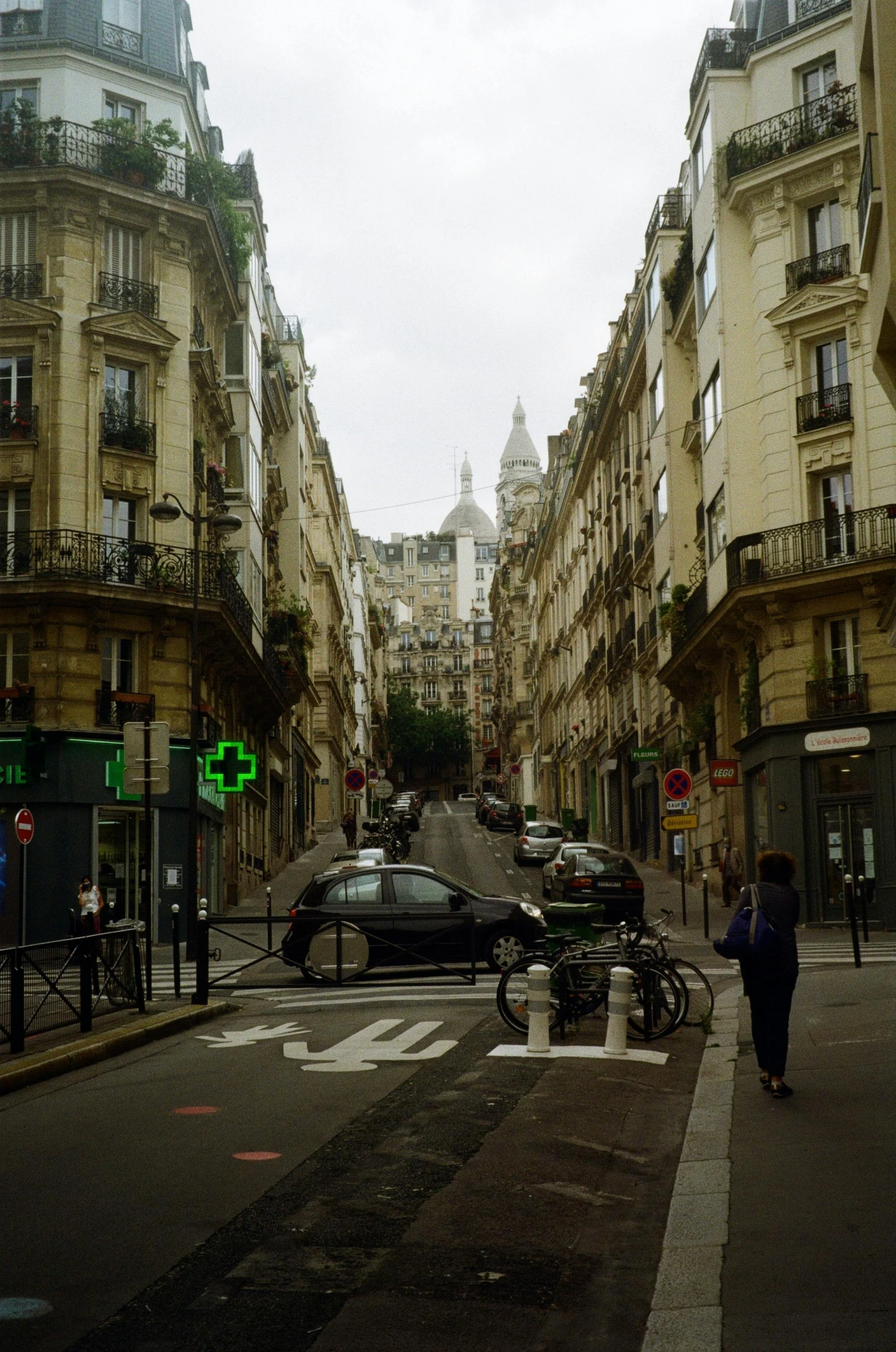 a city street filled with lots of tall buildings, a photo, paris school, gothic city streets behind her, square, medium - shot, neighborhood