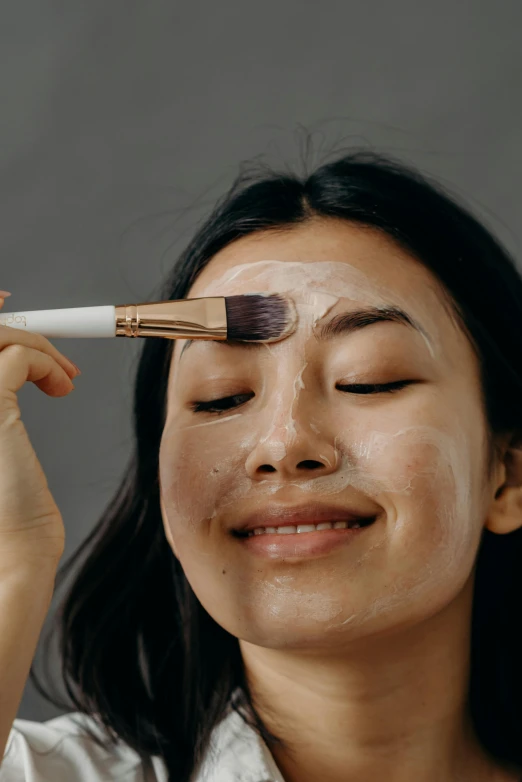 a woman brushes her eyebrows with a brush, by Julia Pishtar, trending on pexels, smiling mask, asian face, face covered in dirt, editorial image