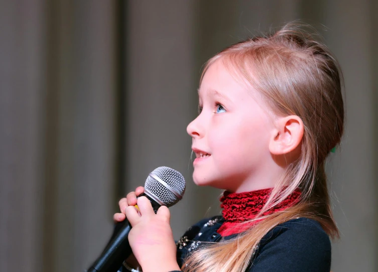 a little girl that is holding a microphone, sitting in front of a microphone