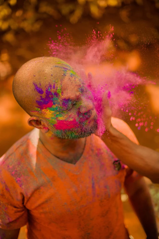 a man with colored powder on his face, bellowing dust, brightly coloured, brown, a man