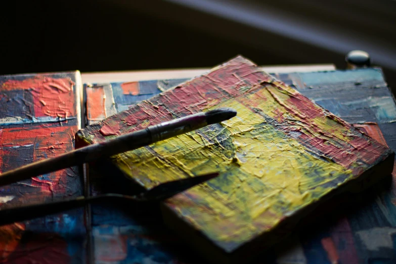 a close up of a piece of art on a table, inspired by Frank Auerbach, unsplash, cigarrette boxes at the table, paint knife, sunlit, multi - coloured